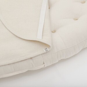 May include: A white round cushion with a removable cover. The cushion has a white fabric cover with a zipper closure and a white label with the text "The Little Green"