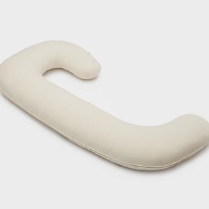 May include: A cream-colored, C-shaped body pillow. The pillow is designed with a curved shape for support and comfort. The pillow is made of a soft, smooth material.