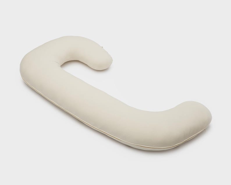 May include: A cream-colored, C-shaped body pillow. The pillow is designed with a curved shape for support and comfort. The pillow is made of a soft, smooth material.