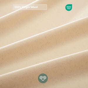 May include: A close-up of beige fabric with soft, flowing folds. The material features a subtle speckled texture. Text on the fabric reads 100% Virgin Wool, accompanied by an OEKO-TEX certification label and a small circular icon of a ram's head.