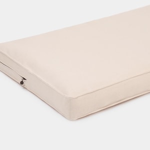 May include: A rectangular, off-white cushion featuring a smooth, solid-colored fabric cover with piped edges. A small, dark metal zipper pull is visible on the side, indicating a removable cover design for this firm, flat-profile furniture pad.