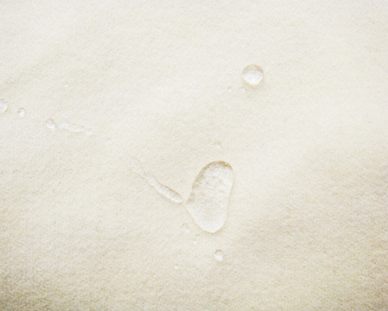 May include: A close-up of a white fabric surface with water droplets. The droplets are round and clear, and they are scattered across the surface.