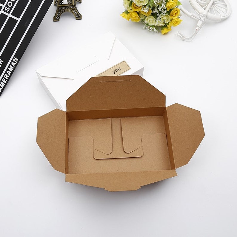 May include: An open, brown cardboard box with a built-in stand. A white box with a label that says "you" is in the background. The box is designed for packaging and presentation.