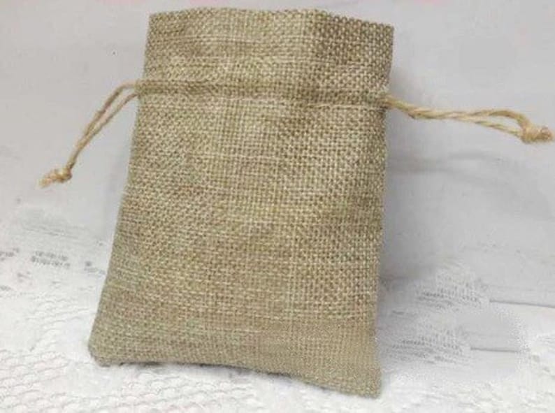 K&ouml;nnte beinhalten: Eine kleine, nat&uuml;rliche Jutesack mit einem hellbraunen Farbton. Die Tasche ist aus einem gewebten Stoff gefertigt und hat ein schlichtes Design.