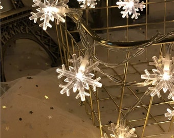 May include: A string of white snowflake-shaped Christmas lights with warm white bulbs, wrapped around a gold wire mesh basket.