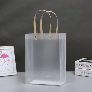 K&ouml;nnte beinhalten: Eine transparente Plastikt&uuml;te mit braunen Papiergriffen. Die Tasche ist leer und hat eine matte Oberfl&auml;che.