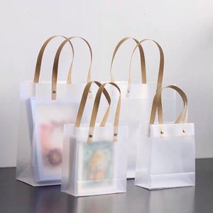 K&ouml;nnte beinhalten: Vier transparente Plastikt&uuml;ten mit braunen Henkeln. Die Taschen sind unterschiedlich gro&szlig; und in einer Reihe vom gr&ouml;&szlig;ten zum kleinsten angeordnet.