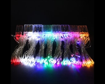 May include: A set of ten battery-operated string lights with different colored LED bulbs. The lights are arranged in a row, with each string having a different color: red, white, blue, green, yellow, purple, pink, and orange. The lights are all turned on and glowing brightly.
