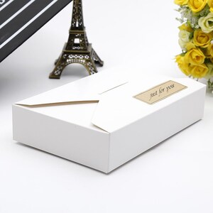 May include: A white gift box with a folded lid and a rectangular label that reads "just for you" in a script font. The box is on a white surface, with a miniature Eiffel Tower and yellow flowers in the background.