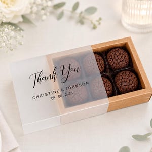 May include: A box of chocolate truffles with a frosted lid. The lid reads "Thank You" with the names "Christine & Johnson" and the date "08.06.2038". The box is brown with six chocolate truffles inside.