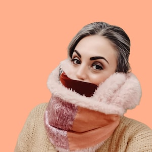 Puede incluir: Bufanda rosa y burdeos con ribete de piel sintética. La bufanda está hecha de un material suave y afelpado y tiene un diseño de patchwork. La bufanda está envuelta alrededor del cuello.