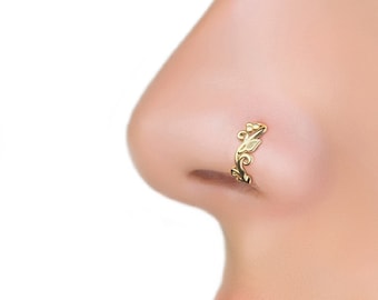 May include: A gold nose ring with a delicate, intricate design. The ring is worn on the left side of the nose.
