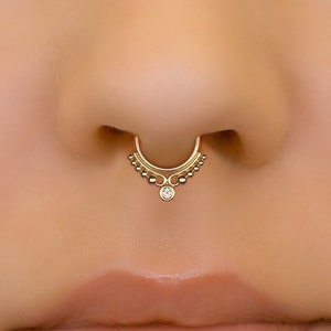 May include: Gold nose ring with a small clear gemstone and a decorative beaded design.