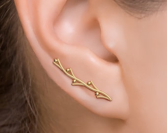 May include: A gold ear cuff with a delicate branch design featuring small round accents. The ear cuff is worn on the upper part of the ear.