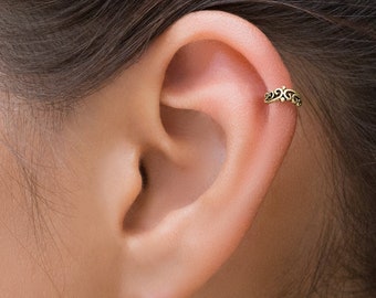 May include: A gold-toned ear cuff with a delicate, ornate design. The cuff is worn in the upper cartilage of the ear.
