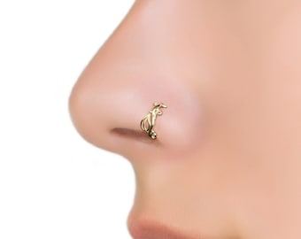 May include: A gold nose ring with a delicate, intricate design. The ring is worn in the left nostril of a person with fair skin.