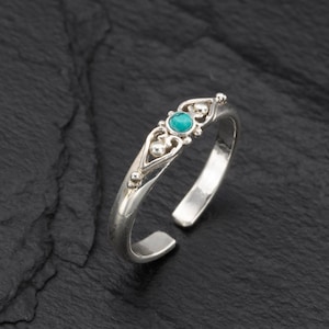 May include: A silver toe ring with a turquoise gemstone set in a delicate, ornate design.