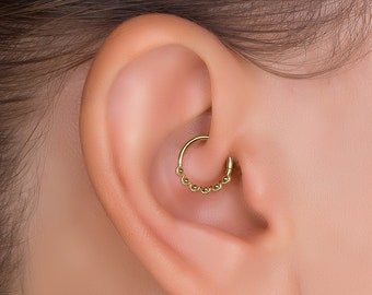 May include: A gold hoop earring with a beaded design. The earring is worn in the upper ear cartilage.