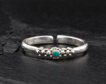Può includere: Un anello per il dito del piede in argento con una pietra turchese incastonata al centro. L'anello è decorato con piccole perline d'argento su entrambi i lati della pietra.
