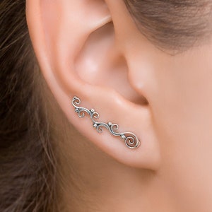 May include: Silver ear cuff with a delicate, vine-like design. The cuff features a series of small, rounded shapes and a spiral at the end.