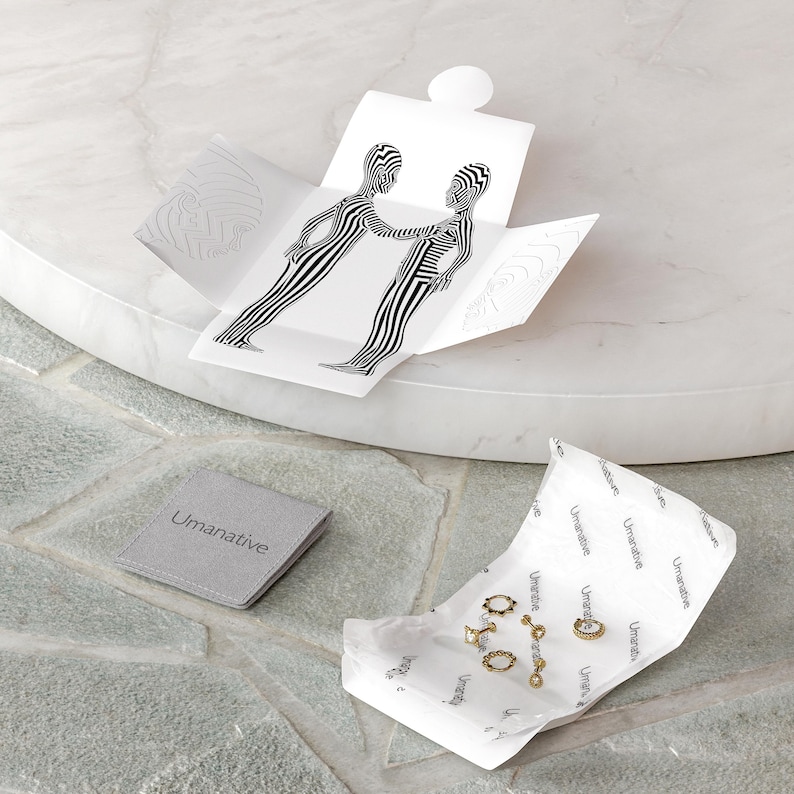 May include: A set of gold hoop earrings and a gold chain necklace with a small pendant, packaged in a white box with a black and white graphic design. The box is open and the jewelry is visible. The jewelry is on a white paper with the word "Umanative" printed on it.