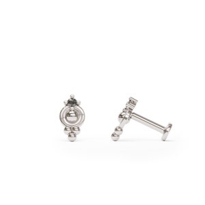 May include: A silver body jewelry piece with a black gem and a circular design. The jewelry is made up of multiple small balls and a larger ball in the center.