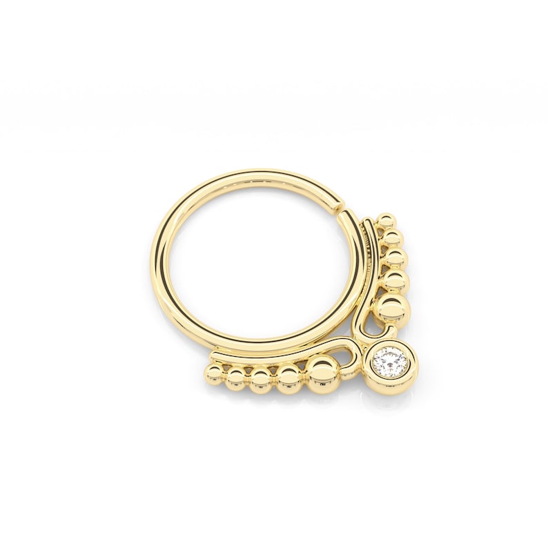 May include: Gold hoop nose ring with a dangling charm featuring a small clear stone and a row of beads.