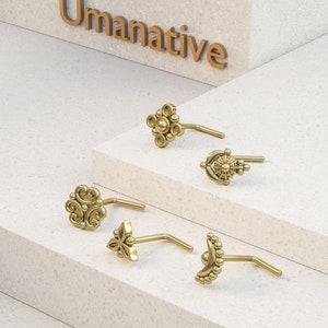 Pode incluir: Cinco argolas de nariz de ouro com diferentes desenhos ornamentados. As argolas est&atilde;o dispostas sobre uma superf&iacute;cie branca.
