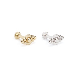May include: Two gold and silver body jewelry pieces with a cluster of small balls on a curved bar. The jewelry is designed for a nose, lip, or ear piercing.