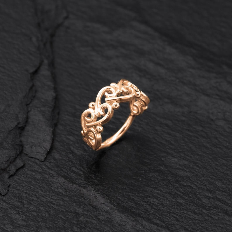 May include: A rose gold filigree ring with a delicate, intricate design. The ring is made of metal and has a smooth, polished finish.