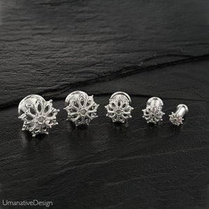 Puede incluir: Cinco expansores de oreja plateados con un diseño floral. Los expansores están ordenados por tamaño, del más grande al más pequeño.