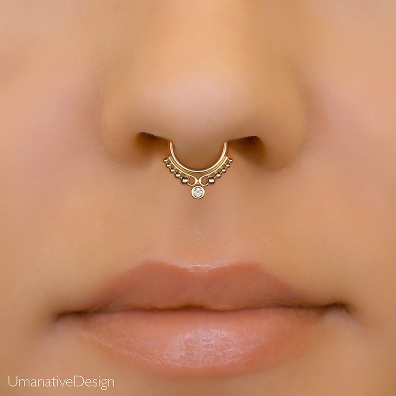 May include: Gold nose ring with a small clear gemstone and a decorative beaded design.