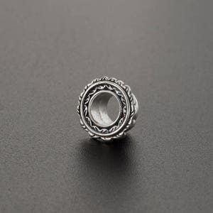 May include: Silver ear gauge with an ornate design around the edge.