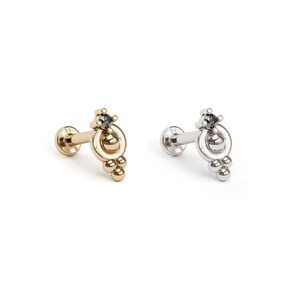 May include: Two gold and silver body jewelry pieces with a small black gem and a cluster of small balls. The jewelry is designed for a cartilage piercing.