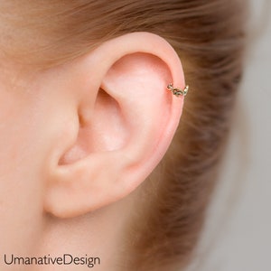 May include: A gold ear cuff with a delicate, ornate design. The cuff is worn in the upper cartilage of the ear.