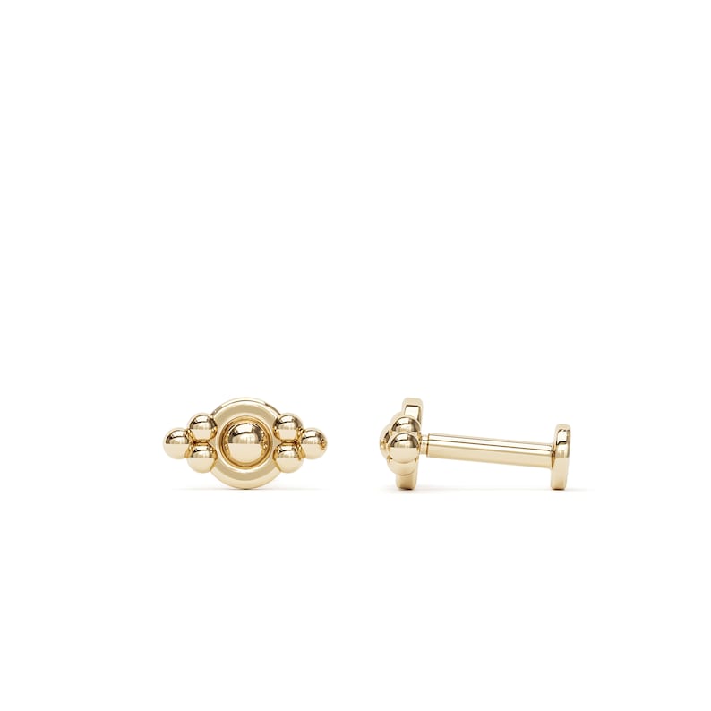 May include: Gold beaded and circular body jewelry, shown in two views. The front view shows a cluster of five beads surrounding a circle. The side view shows a straight post with a bead at one end and a flat back at the other.