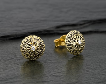 May include: A pair of gold-toned earrings with a delicate filigree design and a small clear stone in the center.