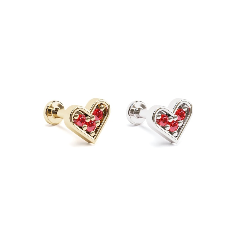 Puede incluir: Un par de pendientes en forma de coraz&oacute;n con piedras preciosas rojas engastadas en un marco de oro y plata. Los pendientes se muestran sobre un fondo blanco.