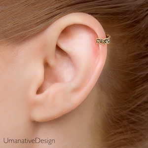May include: A gold-toned ear cuff with a delicate, intricate design. The cuff is worn in the upper cartilage of the ear.