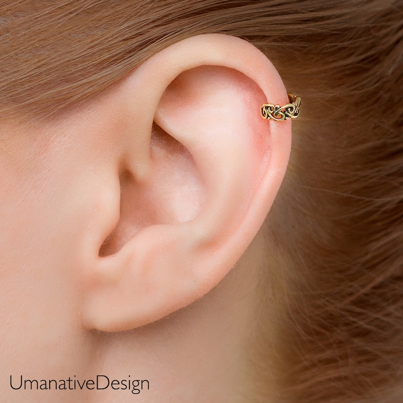 May include: A gold-toned ear cuff with a delicate, intricate design. The cuff is worn in the upper cartilage of the ear.