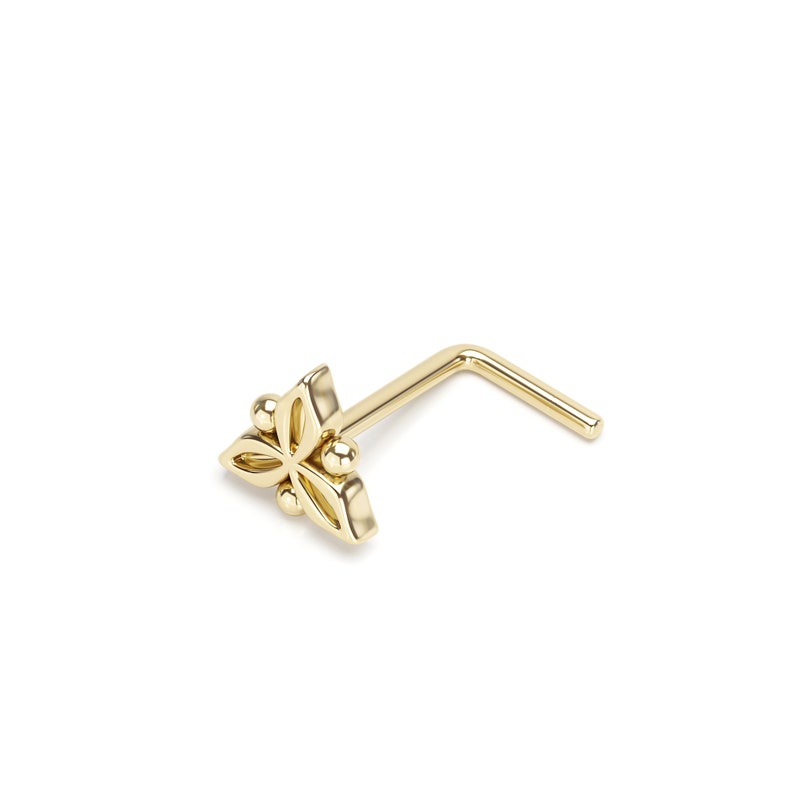Pode incluir: Anel de nariz de ouro com um design de flor. A flor tem quatro p&eacute;talos e tr&ecirc;s pequenas bolas no centro.