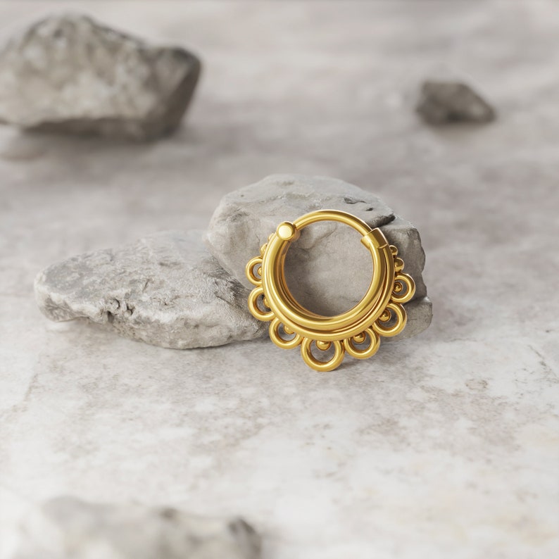May include: Gold septum ring with a decorative design of multiple circles.