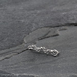 May include: Silver ear cuff with a delicate, swirling design. The cuff is made of sterling silver and has a polished finish.