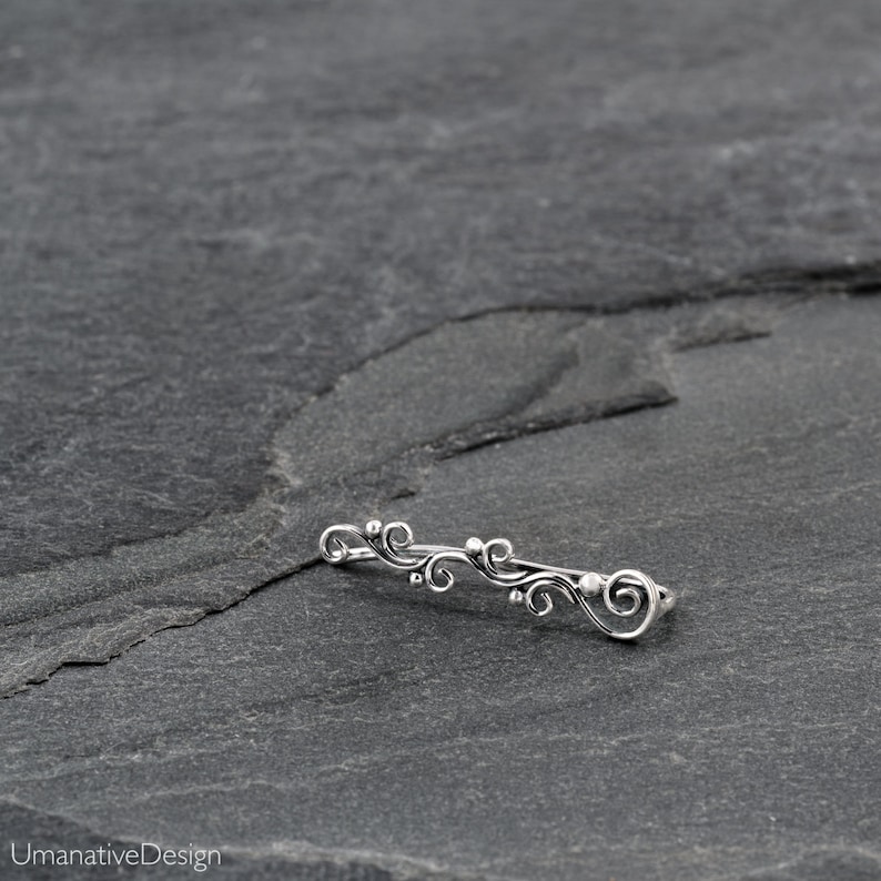 May include: Silver ear cuff with a delicate, swirling design. The cuff is made of sterling silver and has a polished finish.