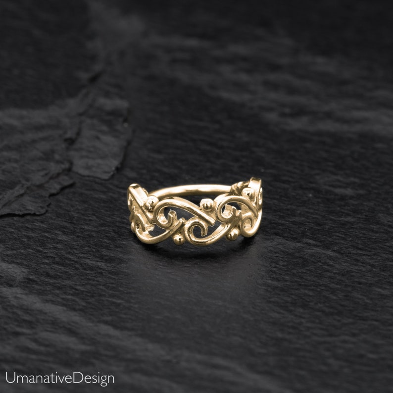May include: Gold nose ring with a delicate, ornate design featuring a series of connected swirls and dots.