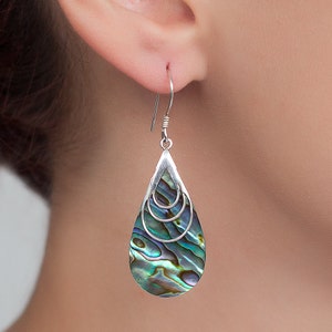 May include: Silver teardrop earrings with a layered abalone shell design. The shell has iridescent green, blue, and purple colors.