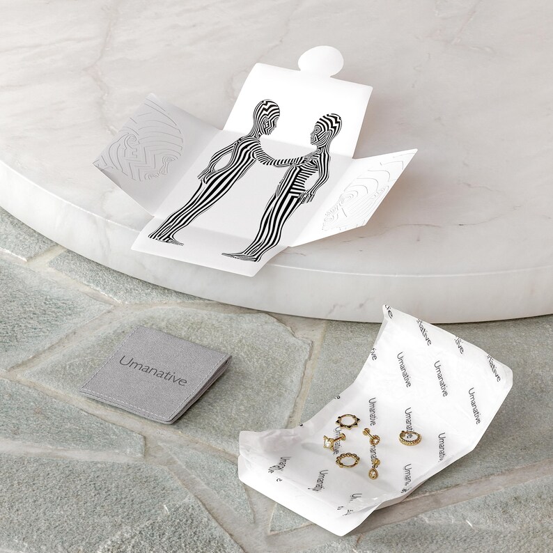 May include: A set of gold hoop earrings and a gold chain necklace with a small pendant, packaged in a white box with a black and white graphic design. The box is open and the jewelry is visible. The jewelry is on a white paper with the word "Umanative" printed on it.