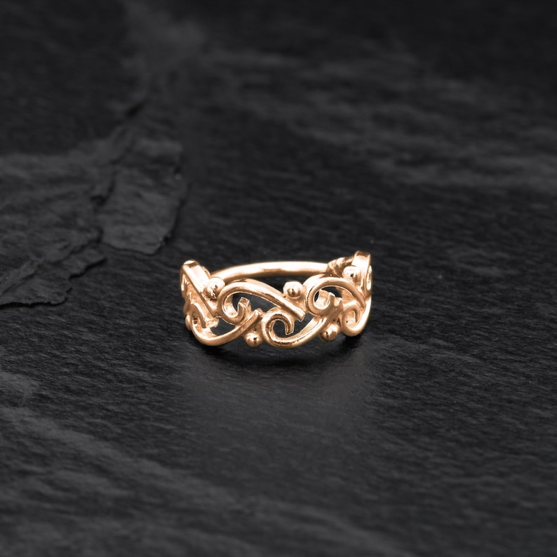 May include: A gold-toned ring with a delicate, intricate design featuring swirling, floral-like patterns. The ring is made of metal and has a smooth, polished finish.