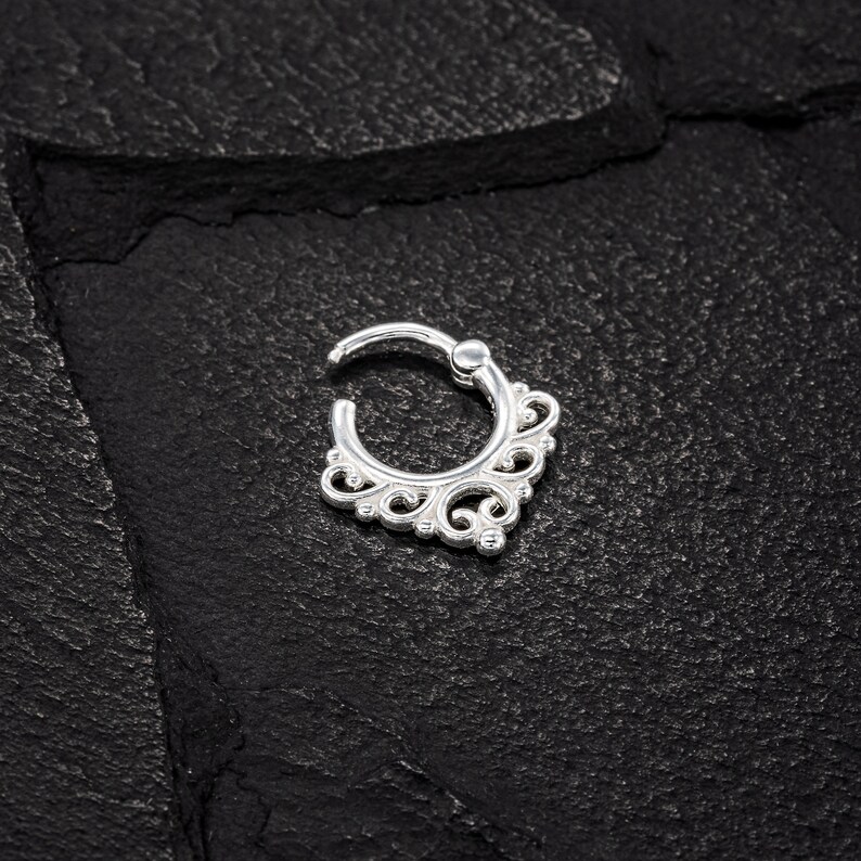 K&ouml;nnte beinhalten: Silberner Nasenring mit einem zarten, verzierten Design. Der Ring ist rund mit einem dekorativen Filigranmuster.