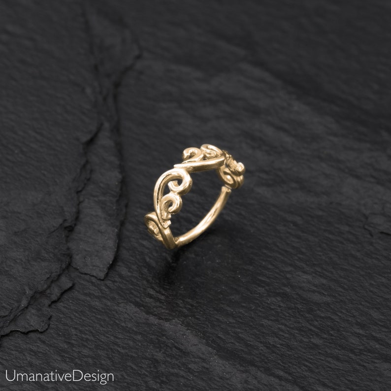 May include: A gold nose ring with a delicate, ornate design. The ring is made of a thin, twisted wire and features a series of small, intricate loops and swirls.